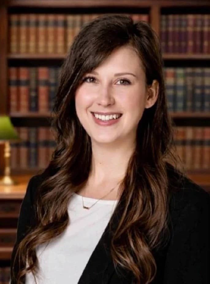 Professional headshot of Rosie Ripley, defense attorney and owner of Ripley Defense, smiling in business attire with a law library background.